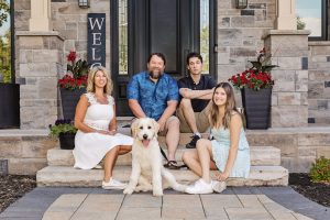 Family with teen kids and dog sitting on front steps of home
