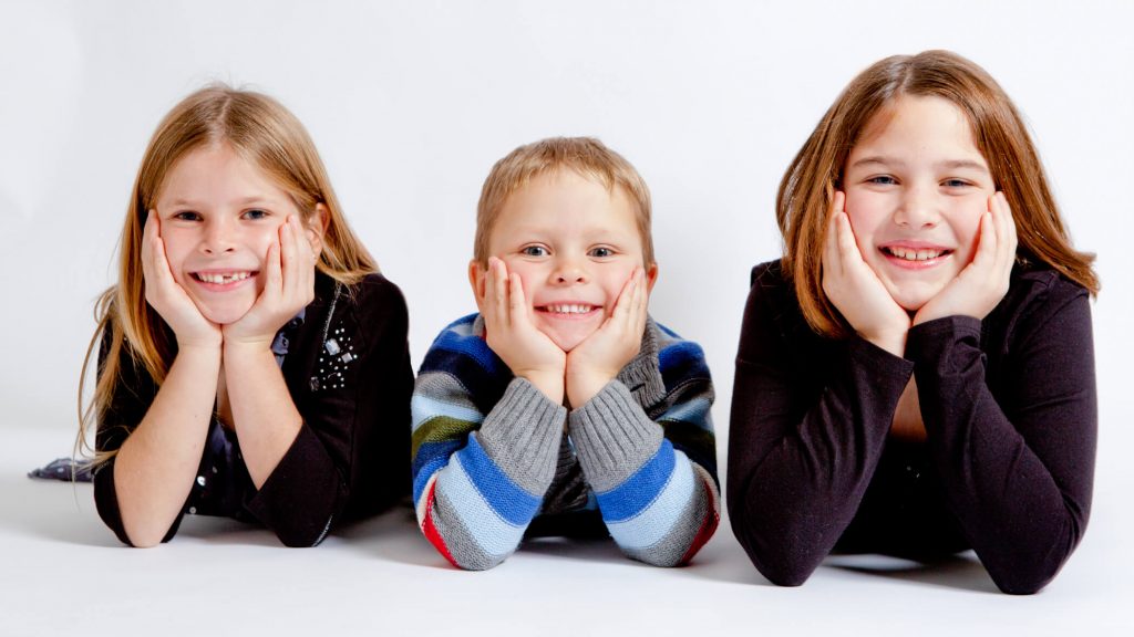 three kids lying on stomachs photographed in studio
