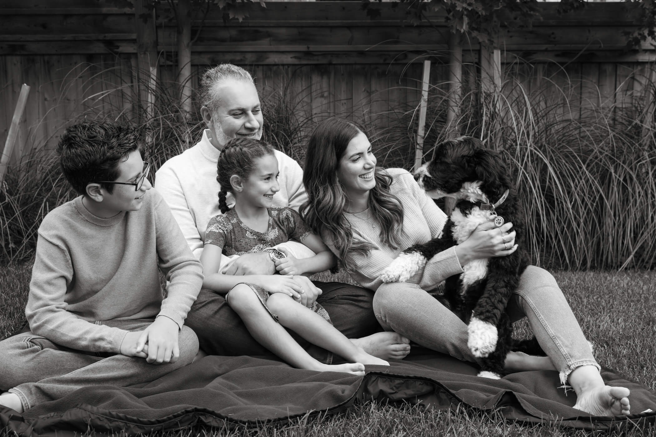 family sits on grass playing with dog in family photo session